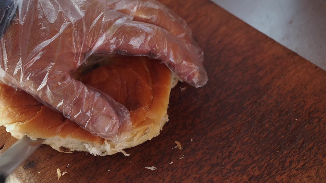 Gloved hand cutting fresh bread on a wooden board