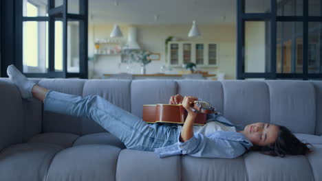 side view of relaxed woman playing guitar in living room