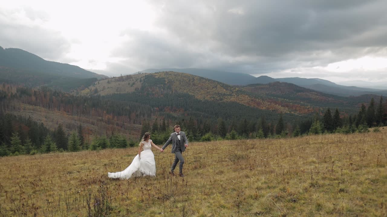 encantadores jóvenes recién casados novia novio corriendo en la ladera de la montaña, tomados de la mano, pareja de bodas familia