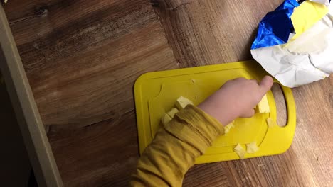 boy cuts butter with a knife on a yellow board, baby help in the kitchen, top view