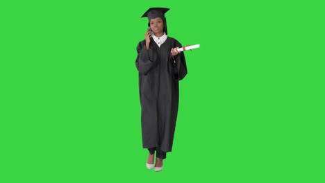 african american female student in graduation robe talking on the phone while walking on a green screen, chroma key