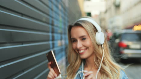 caucasian blonde young woman listening to music with headphones and dancing in the street