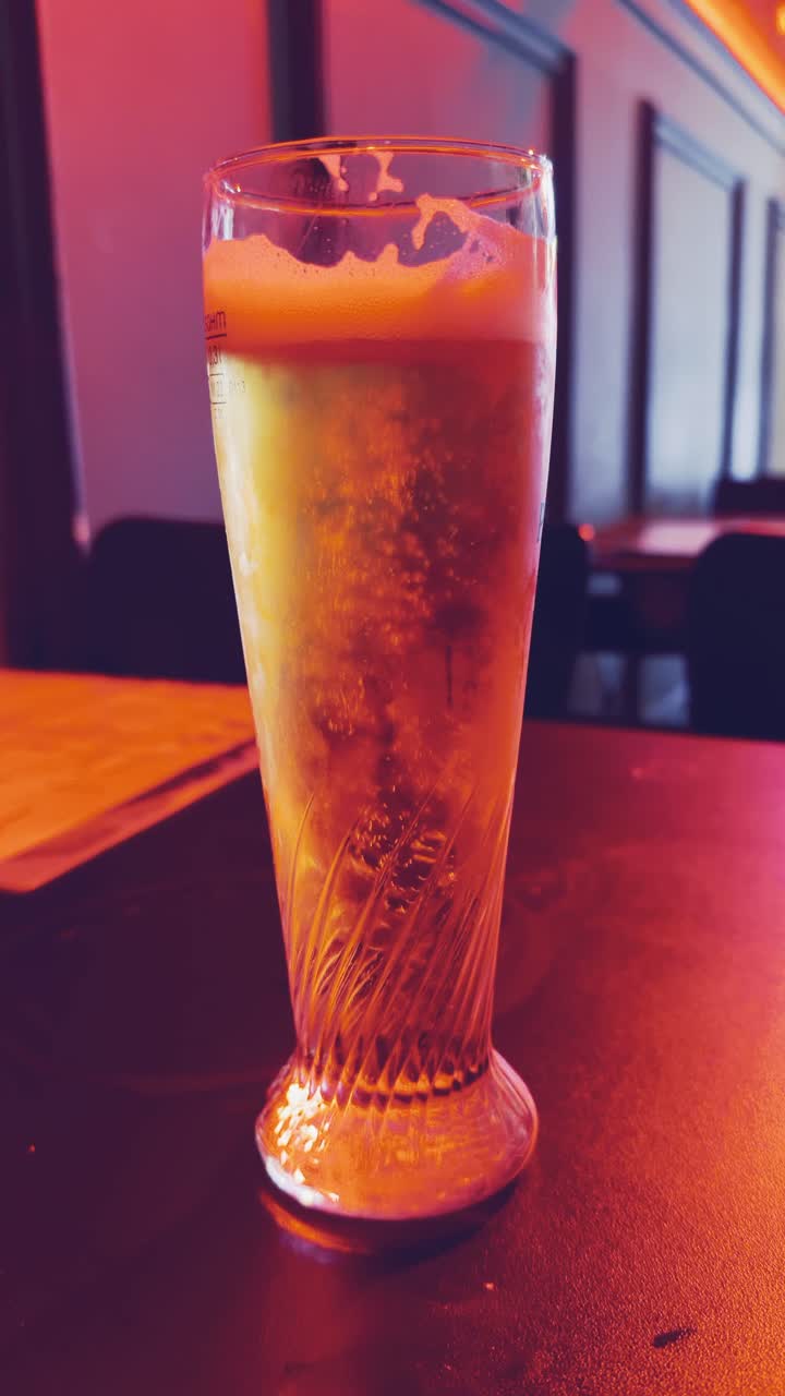 A glass of beer is on a table. The glass is half full and the beer is foamy.