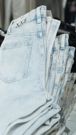 vista en primera persona de una tienda de ropa con vaqueros bien plegados en varios tonos, organizados en estantes de exhibición. arreglo ordenado y variedad de denim disponibles en un entorno minorista moderno