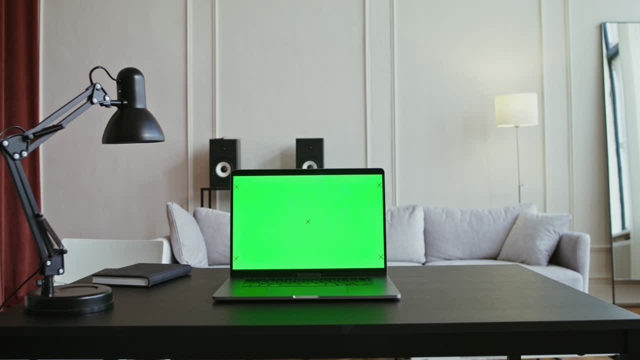 A laptop with a green screen sits on a table in a modern bright interior