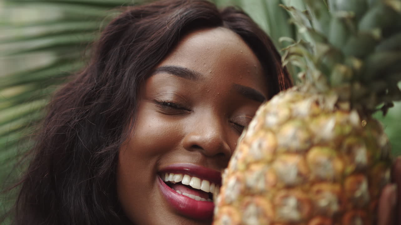 Young beautiful girl with natural makeup holds a pineapple in her hands and smiles at the camera