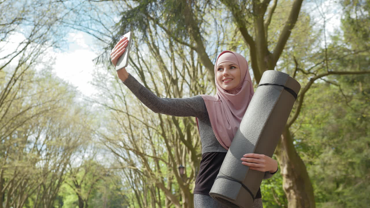 Woman Taking a Selfie in Park While Carrying a Yoga Mat