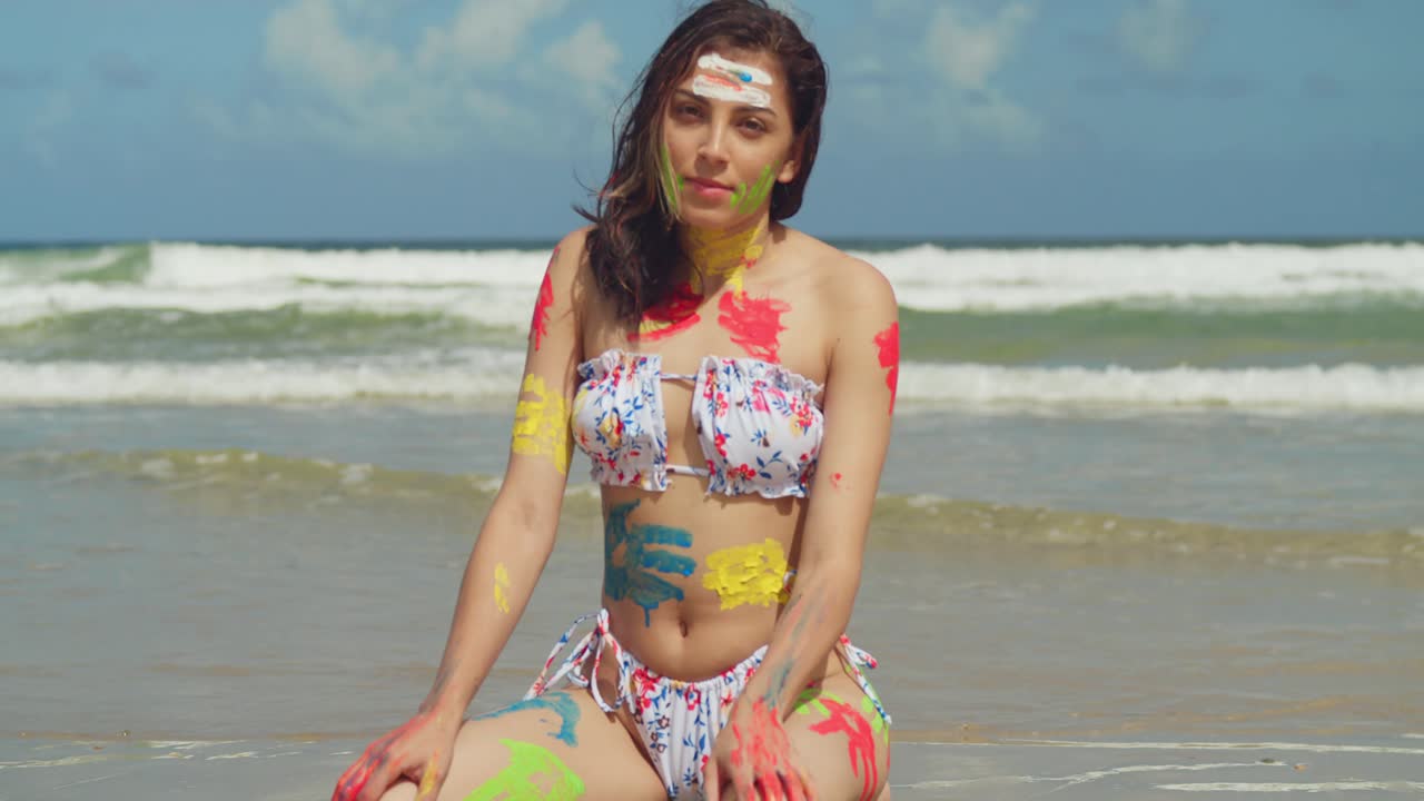 On a bright day in the Caribbean, a girl in a bikini and body paint explores a white sand beach