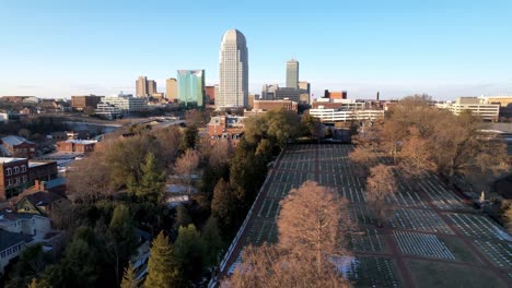 aerial-slow-push-over-bald-cypress-trees-pushing-toward-winston-salem-nc,-north-carolina-skyline