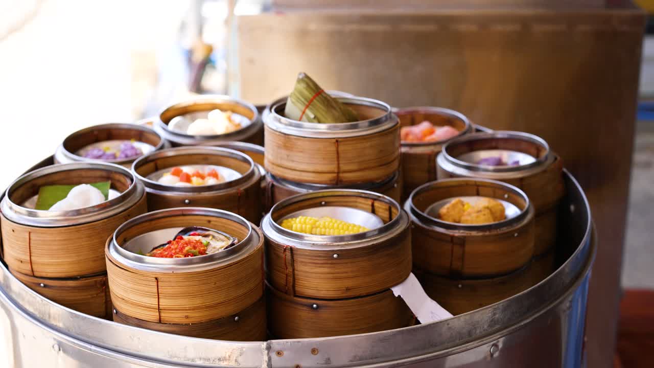 Bamboo baskets filled with colorful dim sum steam in a metal steamer. Bright natural lighting enhances the vibrant scene