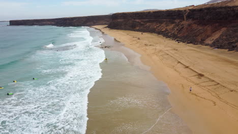 aerial view of a sandy beach washed by the waves, with tourists swimming in the water - escalera, spain