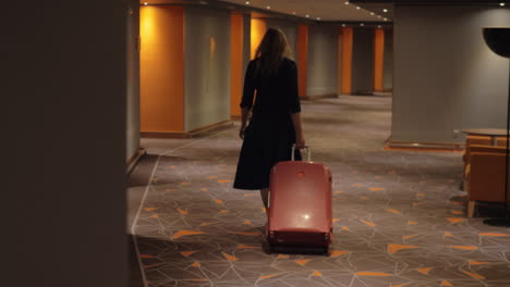 woman with suitcase walking to the room in hotel corridor