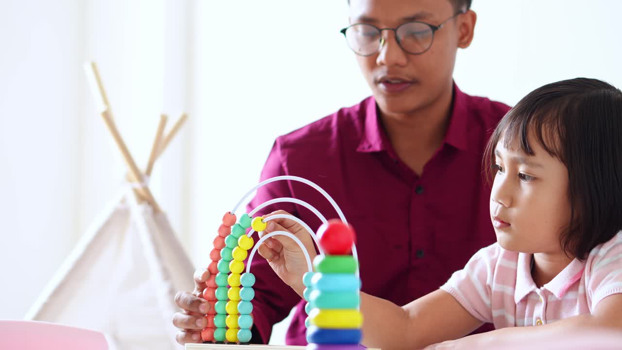 Young tutor in shirt teaches young girl how to count using bead abacus and stacking rings
