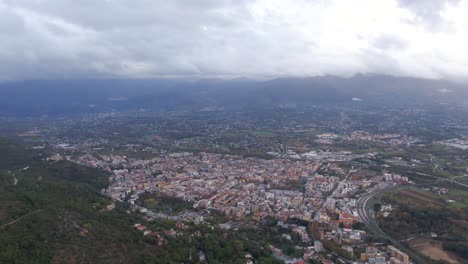 scenic view of downtown cassino city and buildings from green hillside with mountain range in background, italy, sideways aerial