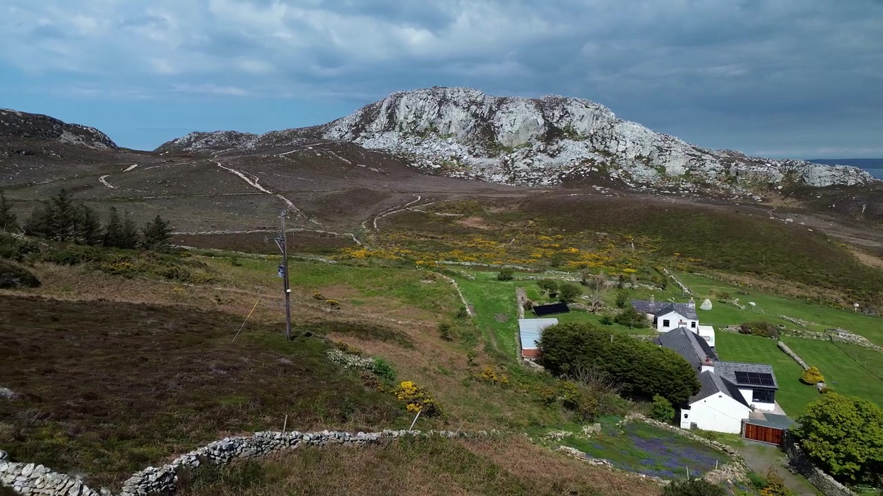 Parallax de vista aérea a través de una casa de campo y un paisaje de páramo en la base de la cumbre de la montaña Holyhead.