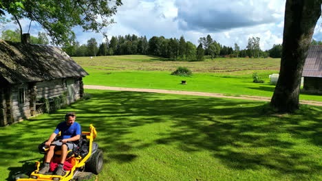 man mowing lawn on farm with log cabin
