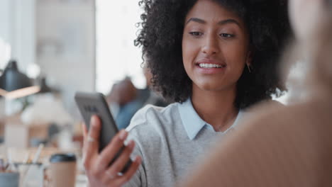 joven gerente de negocios de raza mixta usando un teléfono inteligente entrenando a un pasante señalando la pantalla compartiendo retroalimentación discutiendo ideas con un colega en la oficina
