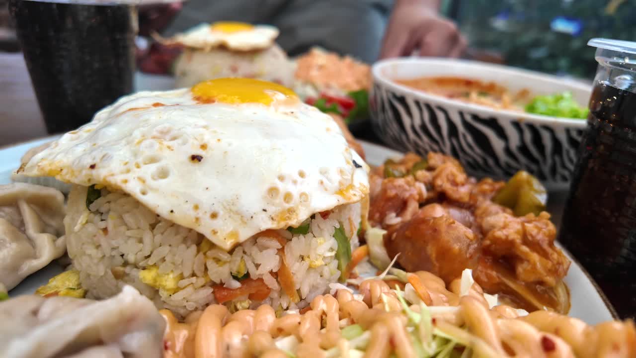 A close-up of a delicious Asian food platter featuring fried rice with a sunny-side-up egg, dumplings, and other dishes