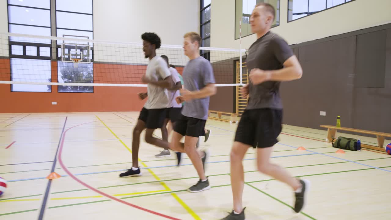 Diverse male teammates reacting to cue, starting footwork drill for warm-up on gym court with cones