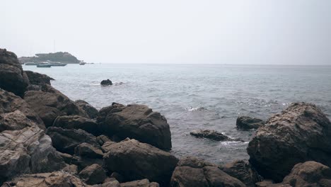 Enormes-Piedras-Grises-De-Playa-Contra-Un-Océano-De-Cristal-Ondulado-Con-Barcos