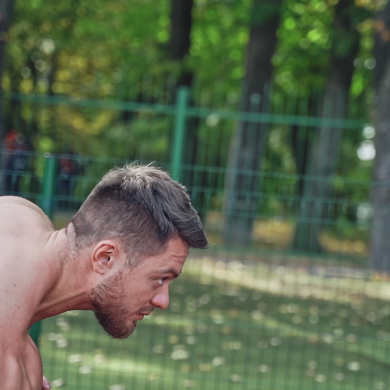Bearded sportsman starts running outdoors. Shirtless young man with muscular body is training in the stadium in summer.