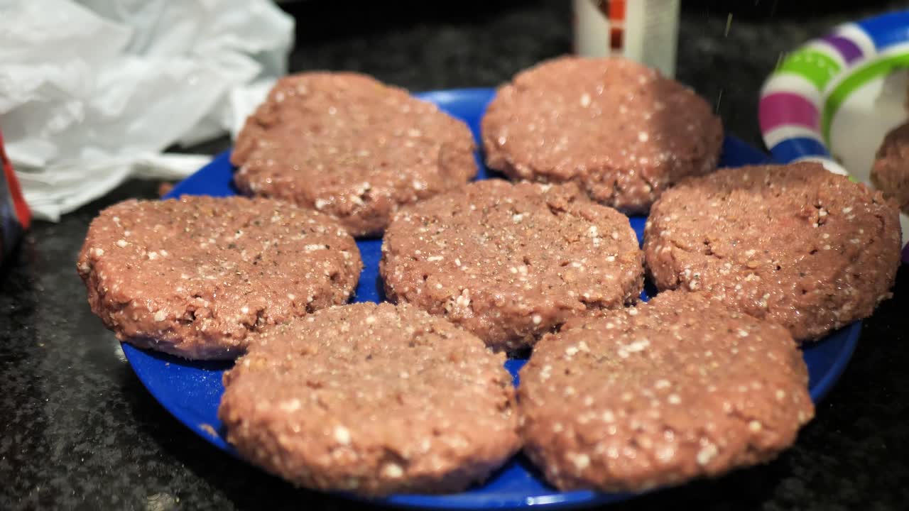 Seasoning plant based burger patties on a blue plate for a summertime barbecue cookout, in slow motion 4k