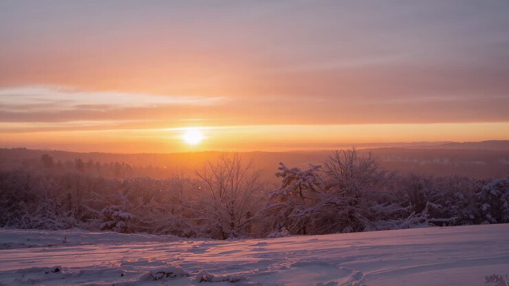 Rising sun casting warm light and brightening snowy hillside with frosted trees and low clouds
