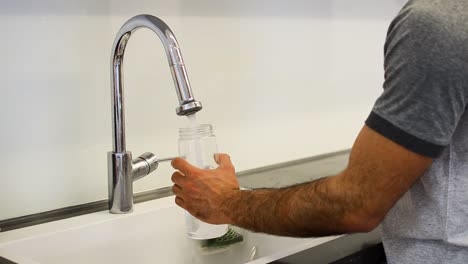 a still shot of a guy filling up a water bottle from the tap next to the counter