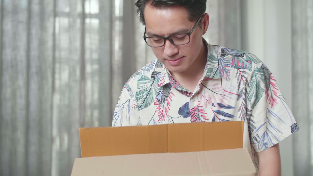 행복한 아시아 남자가 새 집으로 물건을 담은 카드보드 상자를 운반하는 것을 축하합니다.