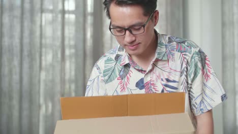 cerca de un hombre asiático feliz celebrando terminar de llevar una caja de cartón con cosas a una casa nueva. él celebra el día de la mudanza