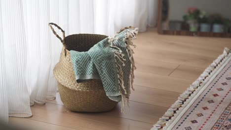 woven basket with green throw blanket on wooden floor by a window