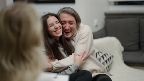 over shoulder - couple visiting psychotherapist office, a man hugs his wife, both smiling