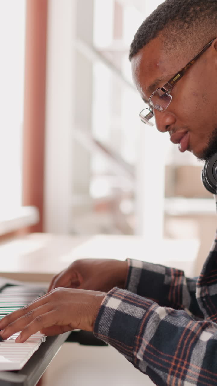 Music creator writes composition on synthesizer. Black man develops musical ideas using electric device at home. African American guy honing musical talents