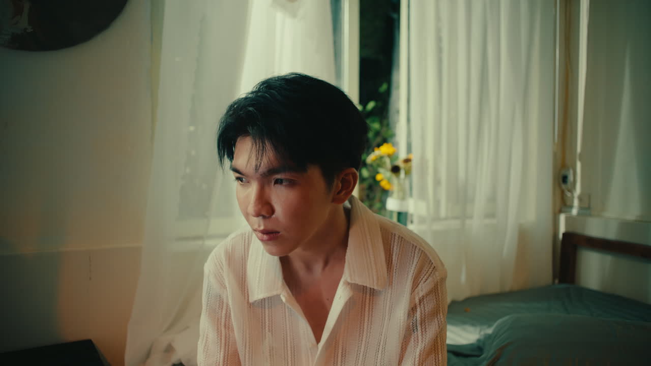 close up of male sitting in bedroom while sad and depressed holding his head in hands