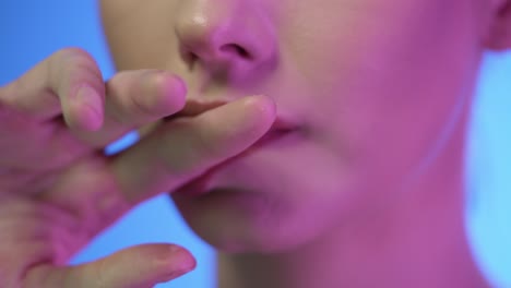 extreme close up of young beautiful woman while she seductively strokes finger over her red full lips with purple contrast on her face in slow motion