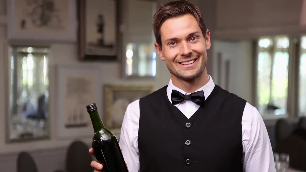 Cameriere bello che tiene una bottiglia di vino rosso