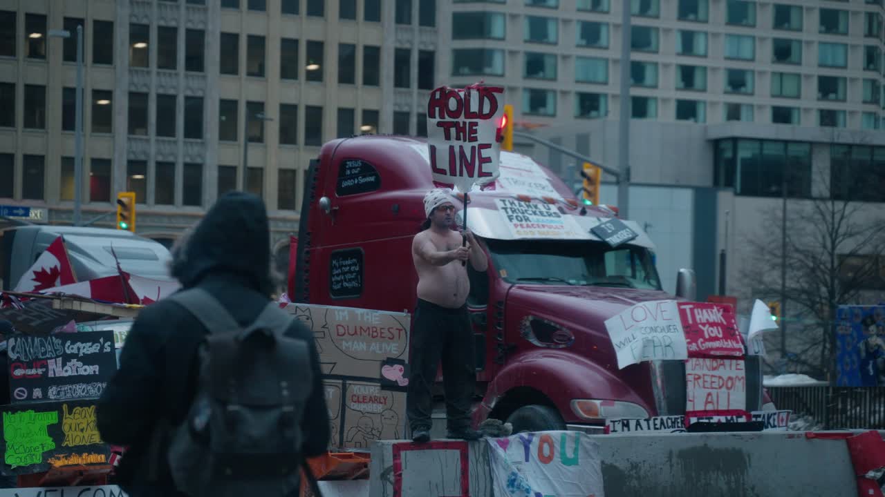 Shirtless Man Holding 'Hold The Line' Sign at a Trucker Protest