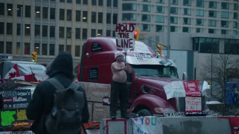 shirtless man holding 'hold the line' sign at a trucker protest