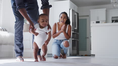 Los-Padres-Animan-A-Su-Hijo-Sonriente-A-Dar-Los-Primeros-Pasos-Y-Caminar-En-Casa.