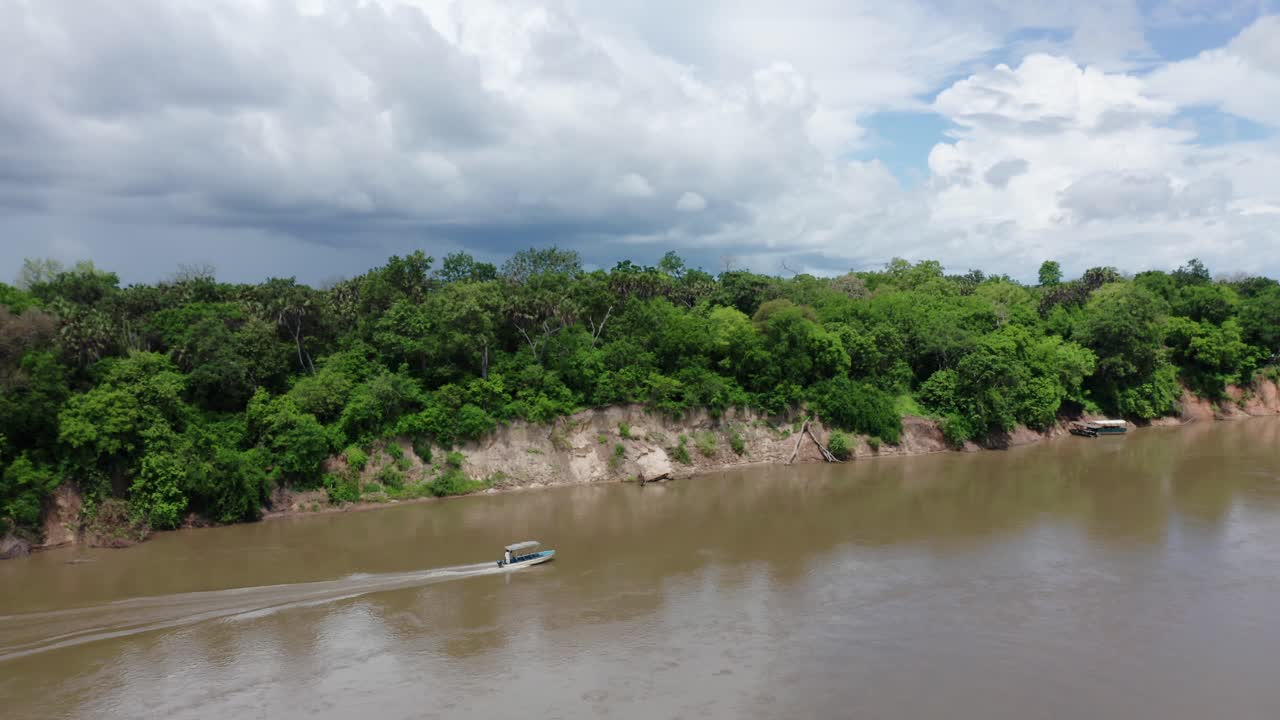 Aerial drone shot flying sideways over a river following a boat going full speed. Selous, Tanzania, cloudy sky