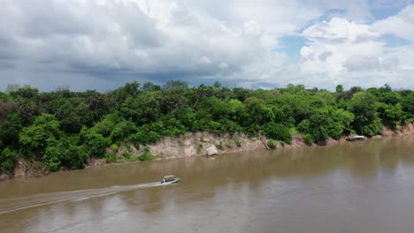 aerial drone shot flying sideways over a river following a boat going full speed. selous, tanzania, cloudy sky