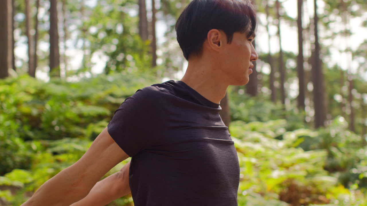 숲 속을 달리는 운동을 하기 전에 몸을 따뜻하게 하고 팔을 펴고 있는 남자의 뒷면 1