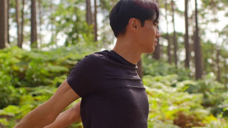 숲 속을 달리는 운동을 하기 전에 몸을 따뜻하게 하고 팔을 펴고 있는 남자의 뒷면 1
