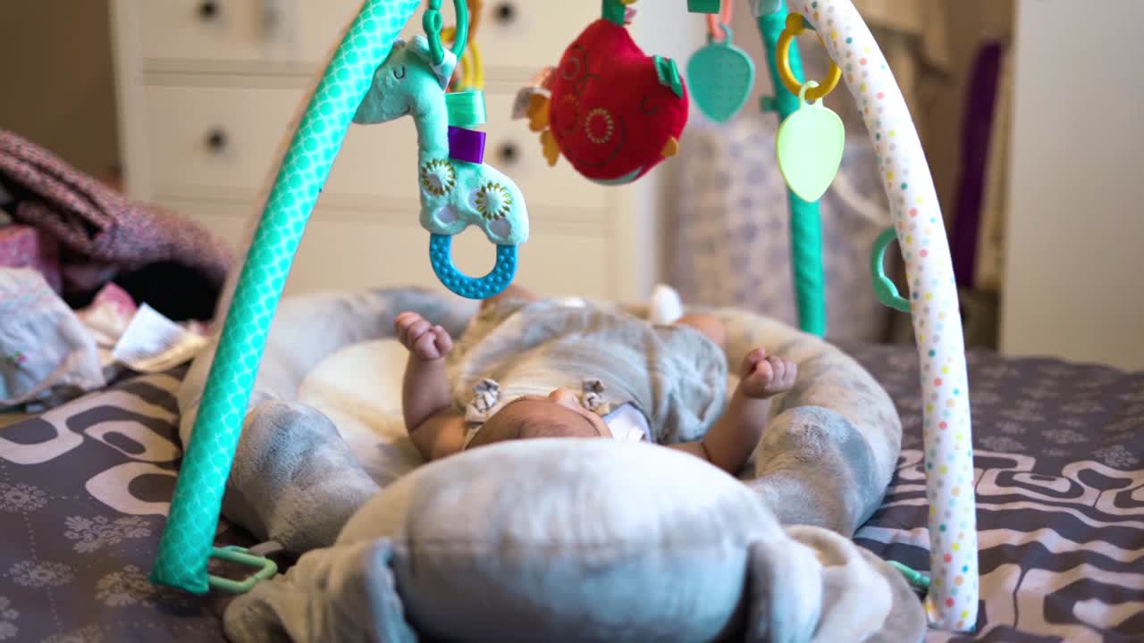 새로운 삶의 개념, 요람에 있는 갓난 아기 소녀가 신기하게 그녀 위에 있는 화려한 장난감을 보고 있습니다