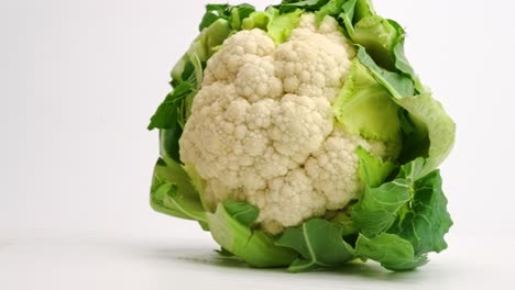 whole head of fresh cauliflower encased in green leaves landing and bouncing on white table top in slow motion