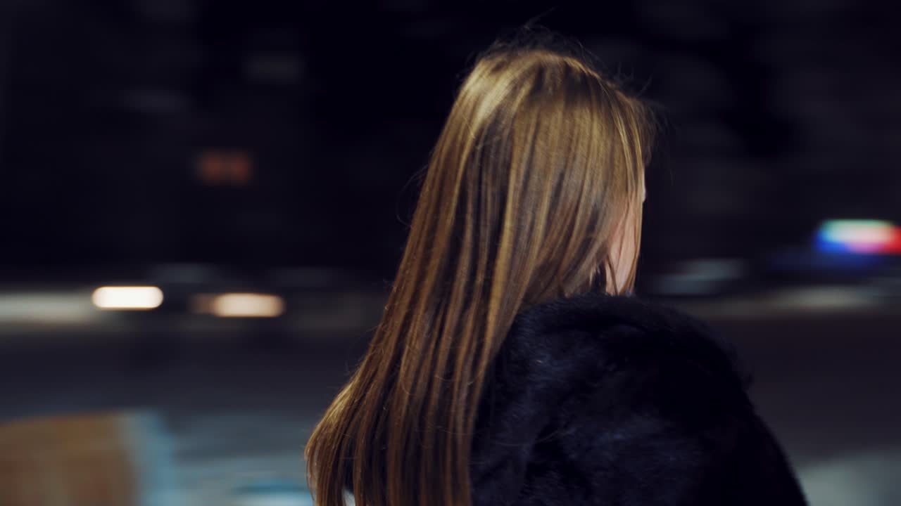 Cute girl with long hair is playing the violin in the square in the city center on the background of evening lanterns. Camera motion to around