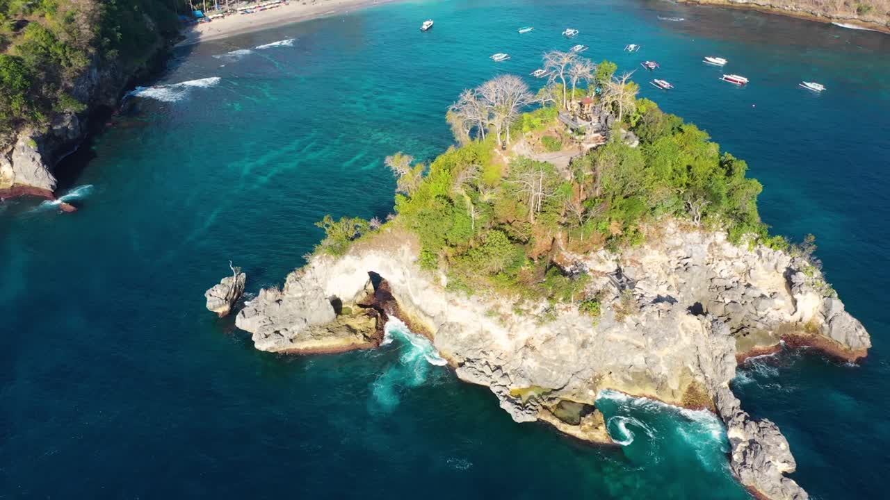 video aéreo cinematográfico de isla tropical con olas de agua turquesa aplastando acantilados rocosos, barcos, costa, playa de crystal bay, nusa penida, bali, indonesia, vista aérea
