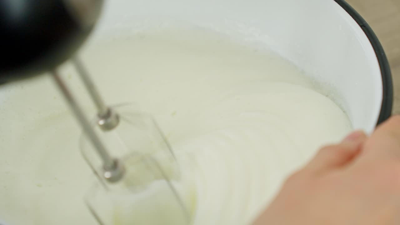 Whipping cream in bowl with hand mixer during tiramisu dessert preparation in kitchen, medium static