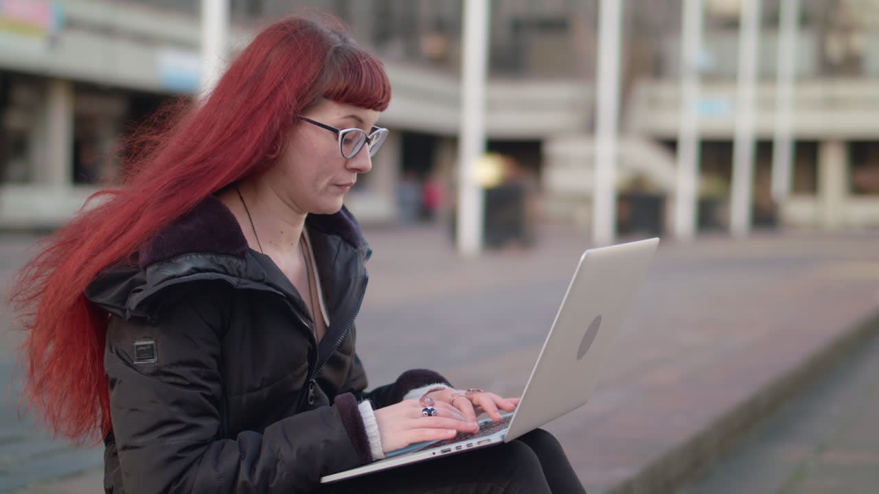 Woman with red hair using laptop outdoors