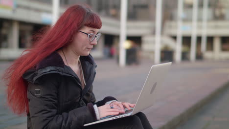 woman with red hair using laptop outdoors